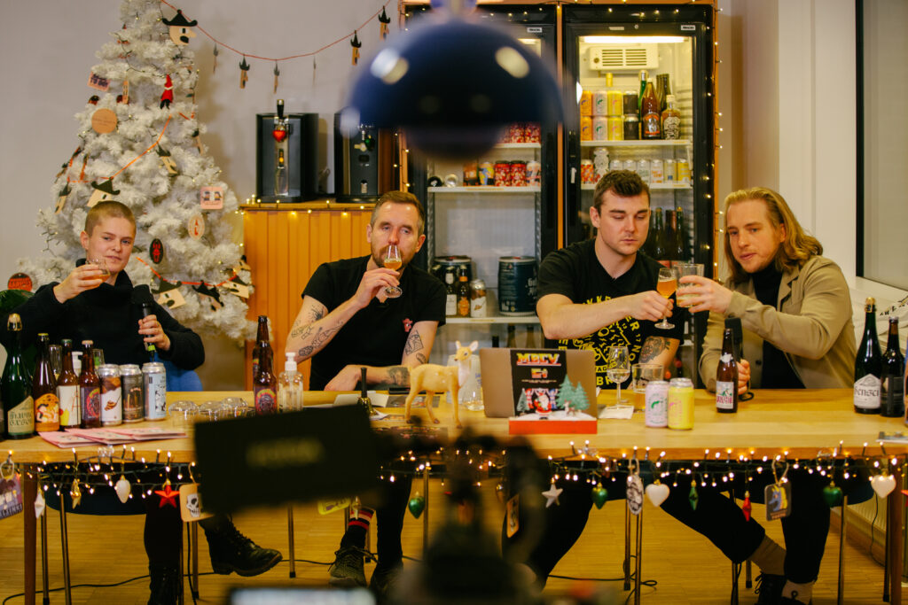 En kvinde og tre mænd sidder i en julepyntet Mikkeller bar og prøvesmager flaskeøl.