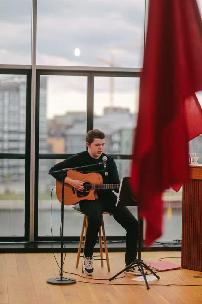 En mand spiller guitar foran en udsigt til Københavns kanaler. I forgrunden hænger en rød fane.