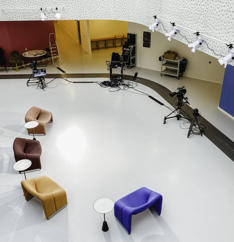 Studiesetup set i fugleperspektiv: Kameraer på stativ peger på gruppe af farvede stole og caféborde.
